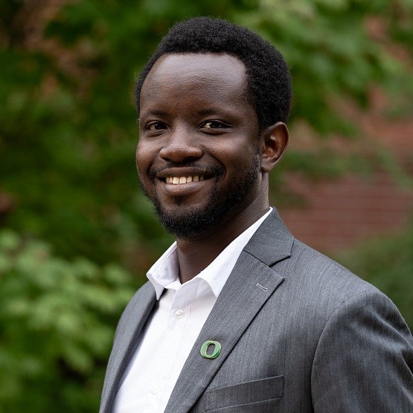 Joel Sati smiles in front of a backdrop of foliage